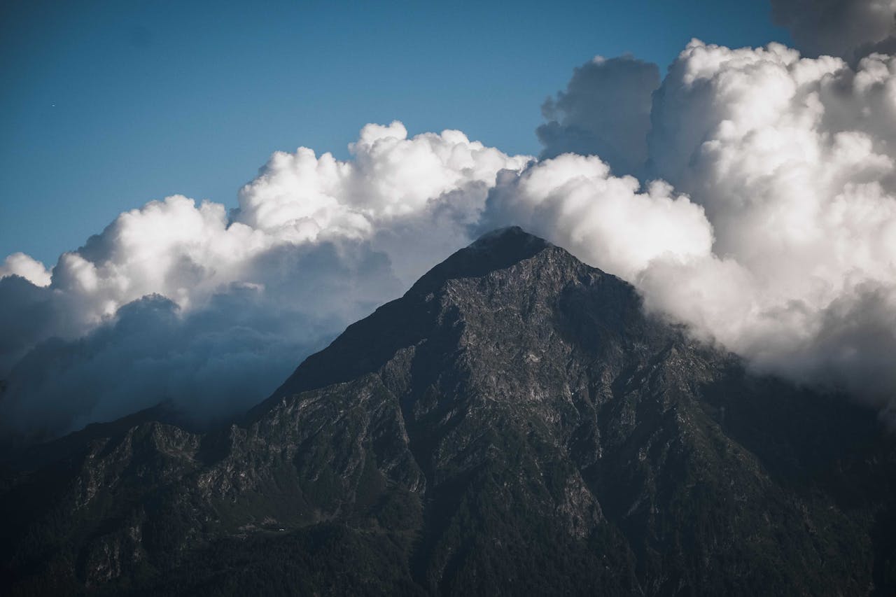 A breathtaking view of a mountain peak surrounded by dynamic, billowing clouds on a clear day.