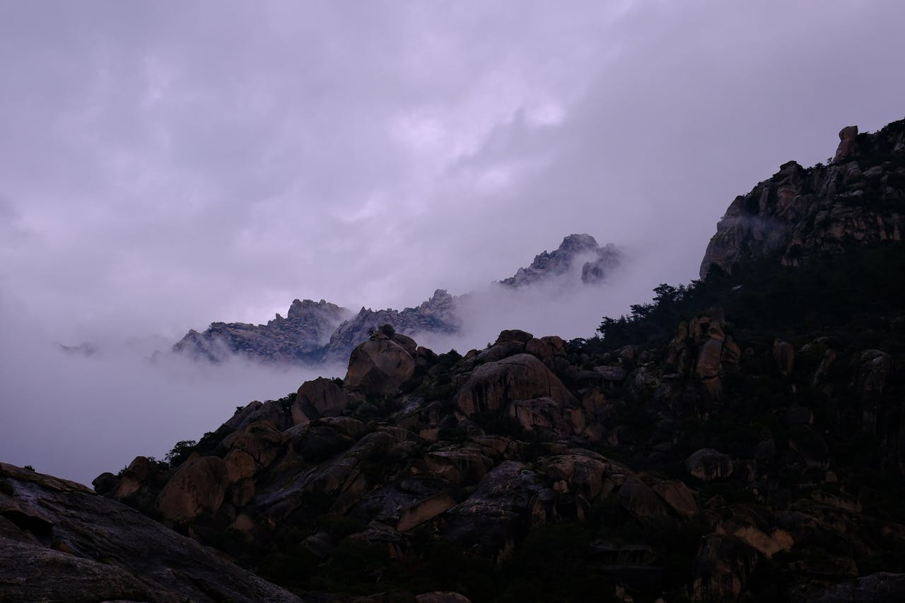 A dramatic view of rocky mountains shrouded in mist at twilight with a mystical ambiance.